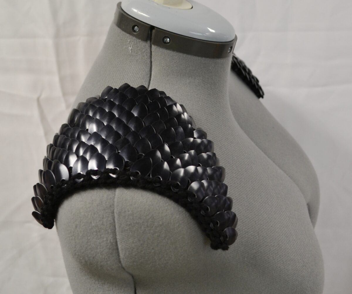 Black scalemaille epaulets, scales pointing in, modelled on a dress form.