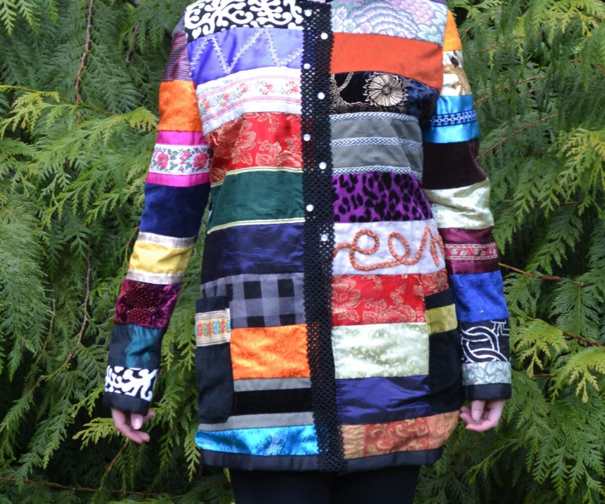 A colorful patchwork jacket with rectangles of differently patterned fabric across the design, modelled by a young woman.