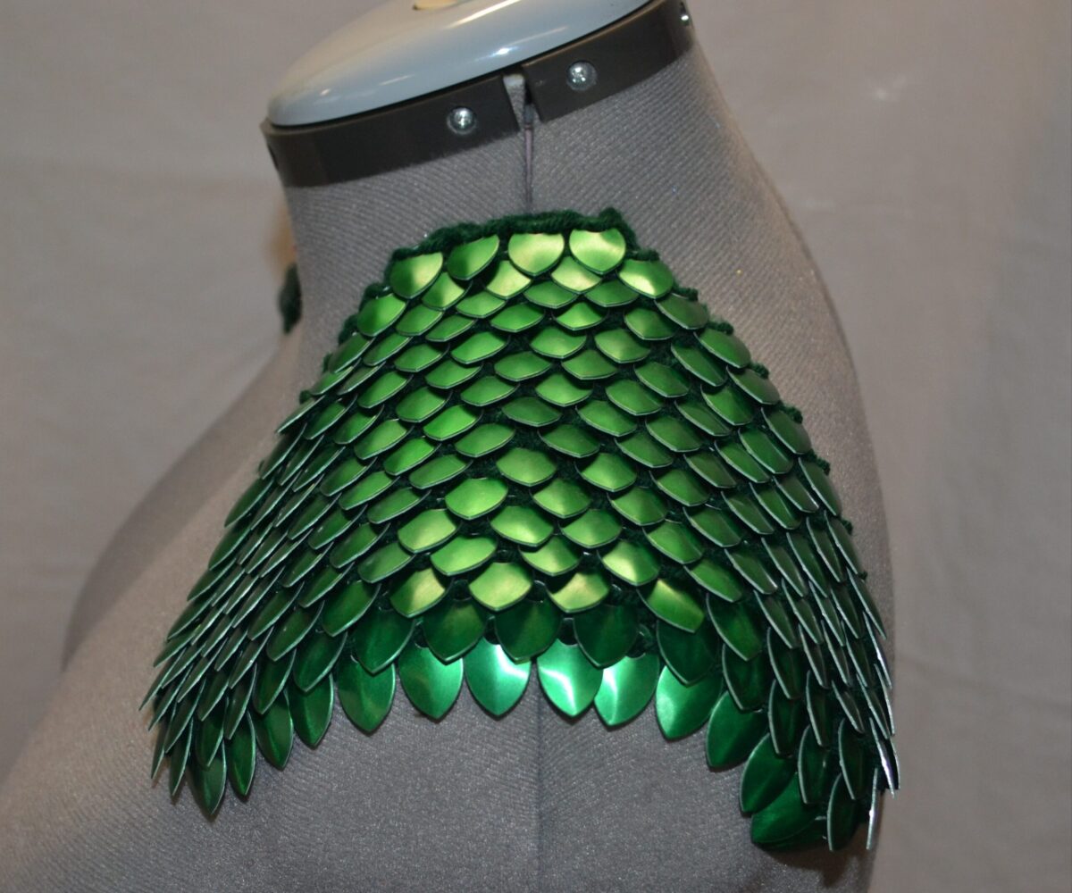 Green knitted scalemaille epaulets, scales pointing outward, modelled on a dress form.