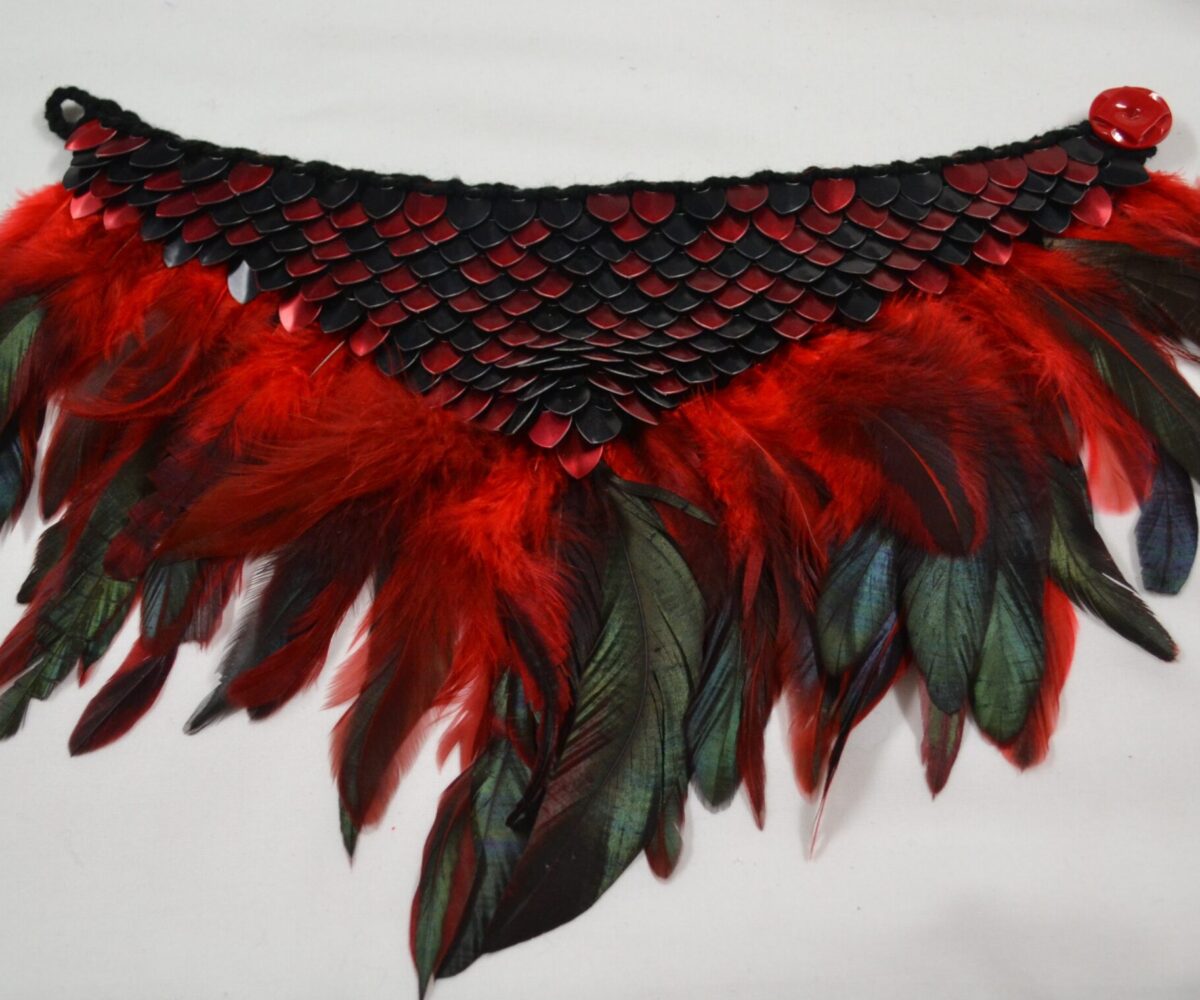 A black and red dragonhide collar with matching feather trim, unbuttoned and lain flat.