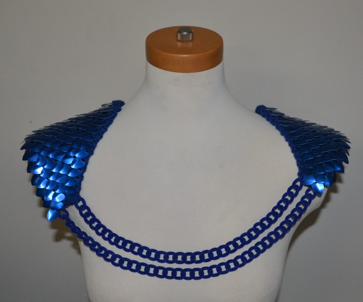 Blue knitted scalemaille epaulets connected by double blue chains, displayed on a mannequin