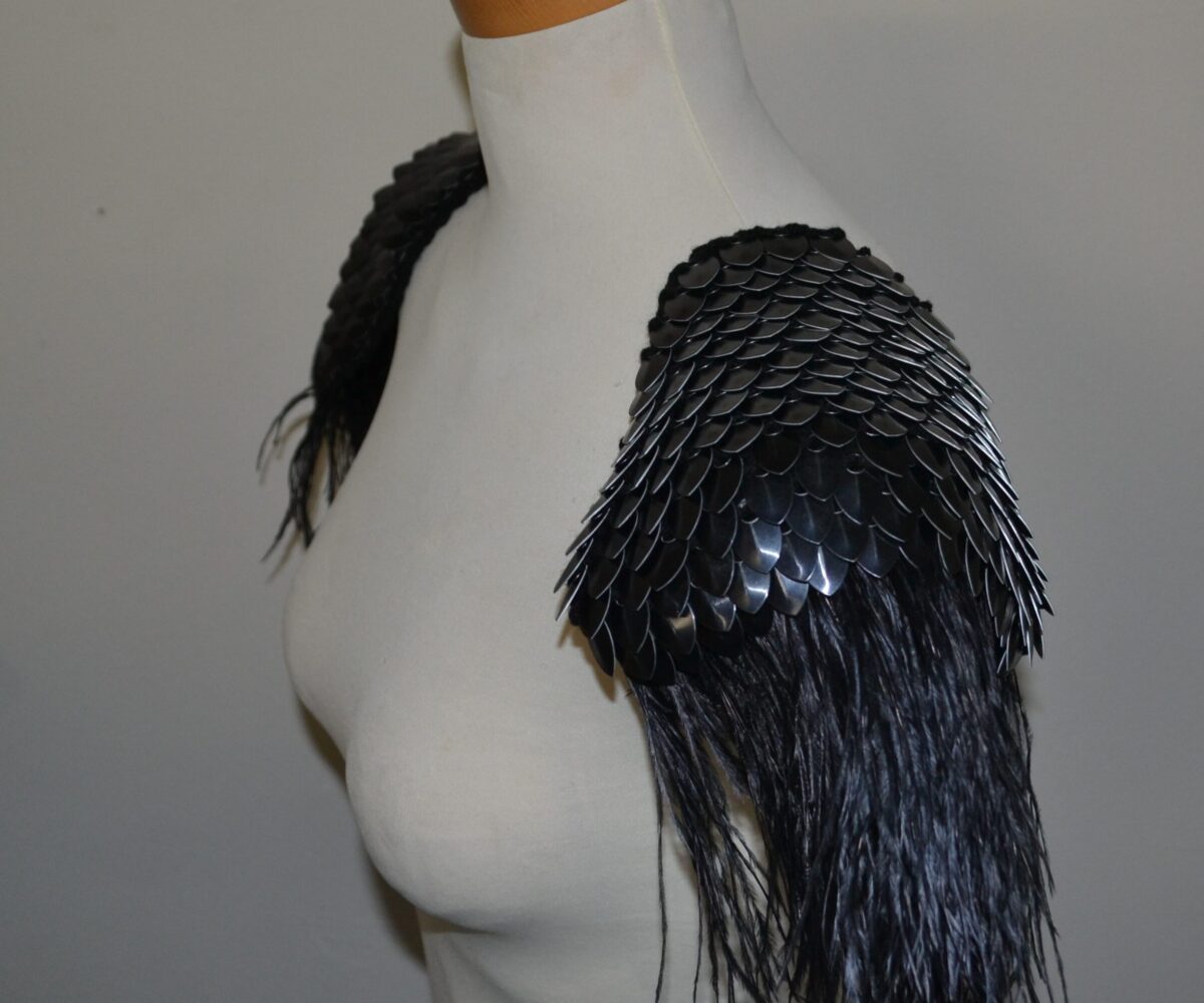 Black knitted scalemaille pauldrons with black feathers cascading down from the shoulders, modelled on a manequinn