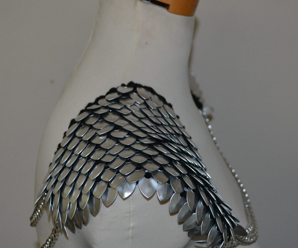 Silver knitted scalemaille epaulets, shown from the side, scales pointing outward, with double silver chains connecting both shoulders.