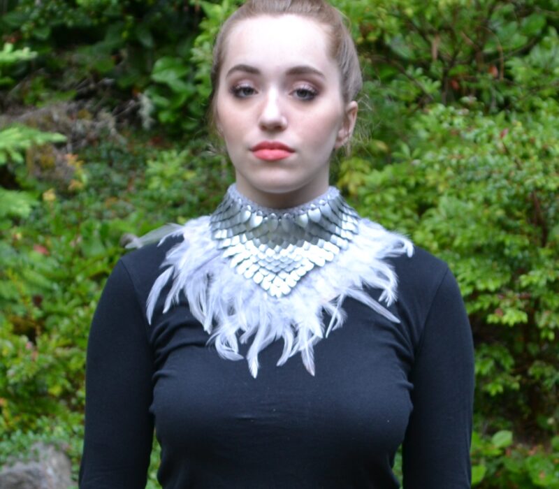 A silver dragonhide collar with white feathers, modelled by a young woman